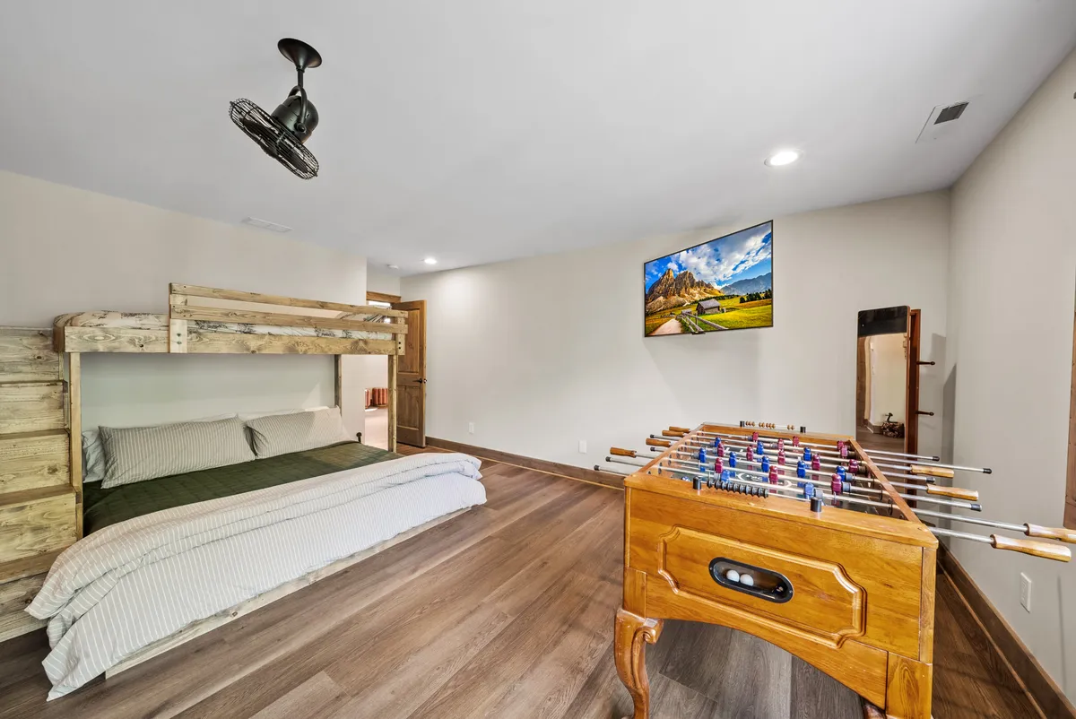 A playful interior shot of a bunk room designed for fun, featuring a bunk bed, a foosball table, a wall-mounted TV, and wooden flooring. The space radiates energy and invites children and teens to enjoy games, storytelling, and bonding time.