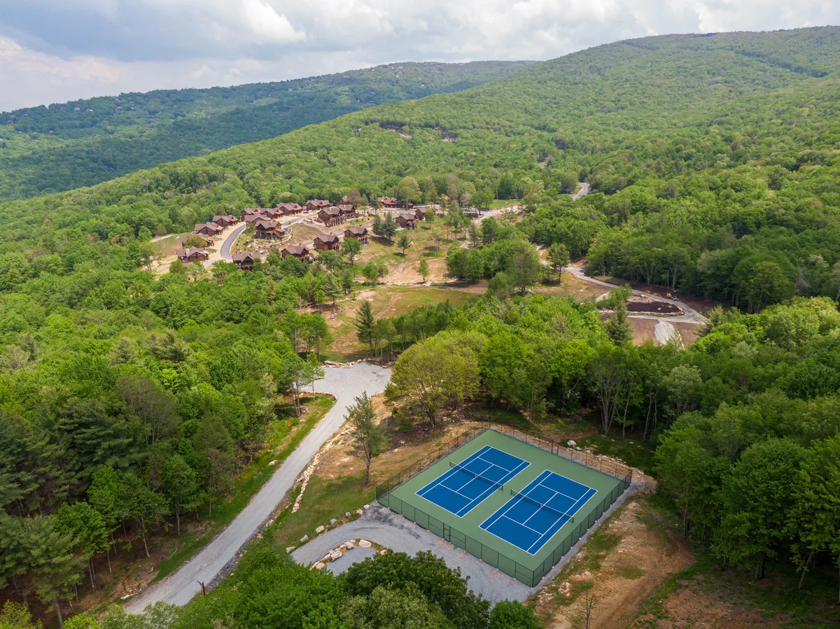 This exterior shot features tennis courts set against a woodland background, with nearby residential buildings. It evokes a welcoming, social atmosphere where guests can enjoy both nature and recreation.
