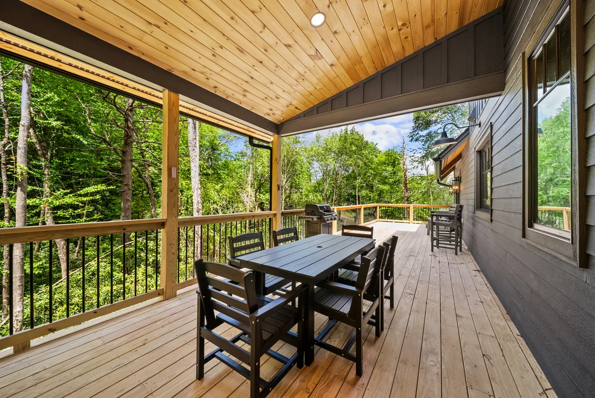 This photo features a wooden outdoor dining table surrounded by trees, with a grill nearby. The environment is serene and inviting, perfect for outdoor gatherings, meals, or simply spending time in nature with loved ones—including furry friends.