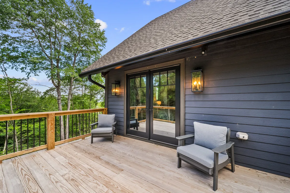 This image captures a wooden deck with outdoor seating, positioned to overlook the surrounding nature. The deck is attached to the house via sliding glass doors, and the area is bathed in natural light, suggesting a peaceful spot for relaxing with pets while enjoying the outdoors.