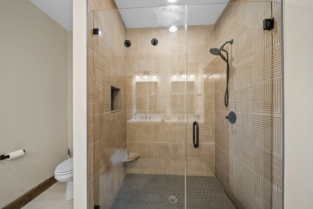 A modern, spa-like ensuite bathroom with a glass shower enclosure, textured wall tiles, and sleek dark fixtures. The clean, refreshing space offers a sense of rejuvenation and luxury after a long day.